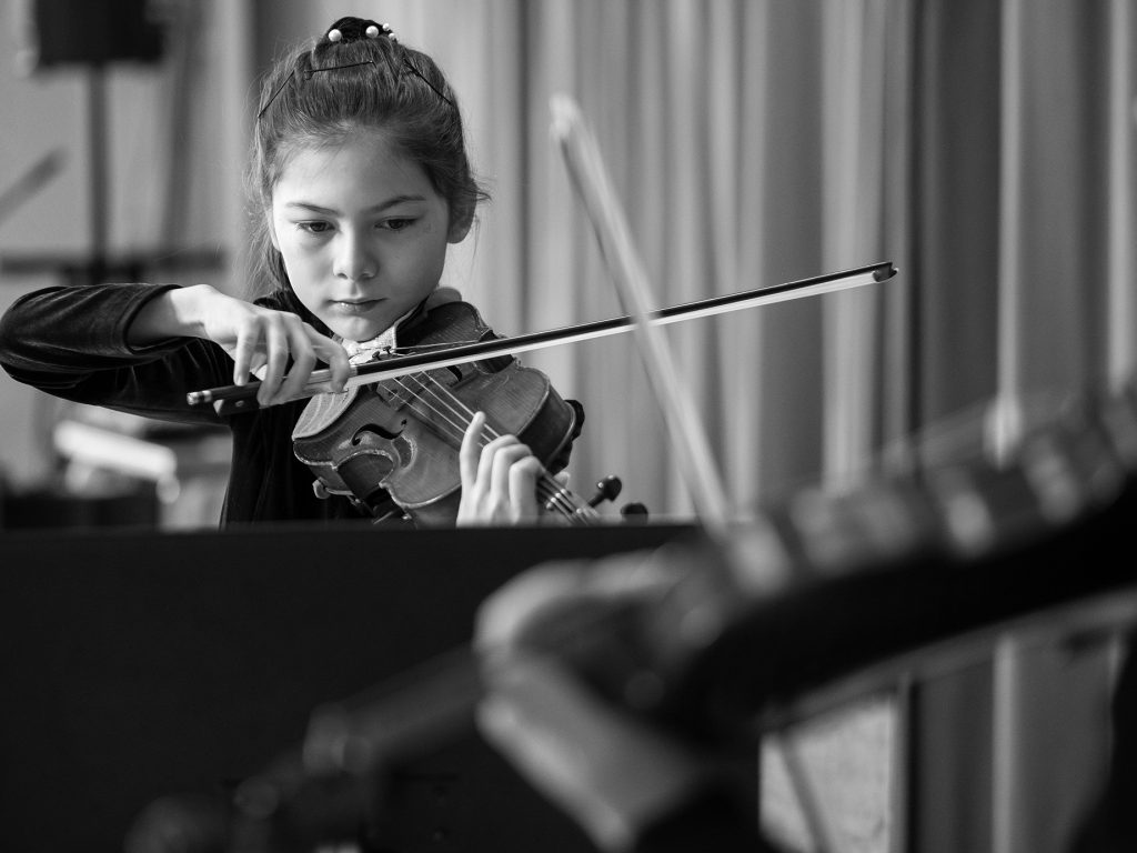 Ung tjej spelar fiol, i förgrunden ser man en instruktör som spelar fiol.